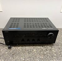 Front view of ONKYO TX-8050 stereo receiver showing control buttons, volume knob, power button, headphone jack, and ONKYO logo with power cable.