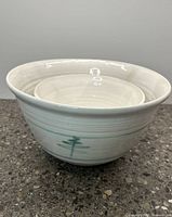 Two ceramic mixing bowls stacked inside each other showing the green tree and mountain painted design on white ceramic.