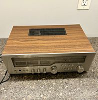 Angle view of the receiver showing wood veneer top and front panel with knobs and tuning display.