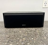 Front view of Sony SS-CN200AV center speaker on a grey stone surface, showing black fabric grille with Sony logo.