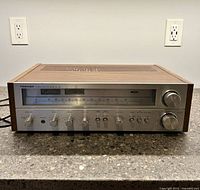 Front view of Toshiba SA-725 stereo receiver on countertop showing its wooden side panels and metal face with control knobs and meters.