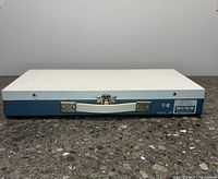 Front view of closed slide sorter case showing white top and blue bottom with handle and latch.
