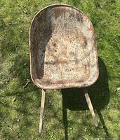 Top-down view of a rusty metal wheelbarrow with wooden handles on grass.