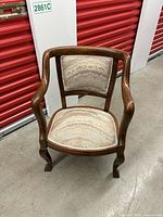 Front view of antique wooden side chair showing wooden arms, carved legs, and patterned upholstered seat and backrest.