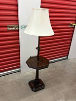 Full view of antique table lamp with cream fabric shade and dark wood column and base.