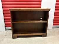Front view of two shelf wooden bookcase with solid wood construction and a small hole in the back panel.