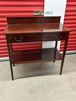 Front view of cherry wood sideboard with drawer and brass handles.