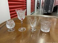 Four different types of pinwheel crystal glasses on a wooden table: brandy glasses, short wine glasses, drinking glasses, and long stemmed wine glasses