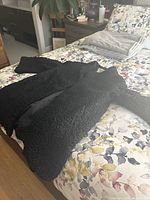Black long fur coat laid flat on bed, showing full length and sleeves.