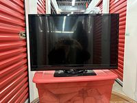 Front view of the 27-inch Insignia TV with its black pedestal stand, screen turned off, located in a storage unit.
