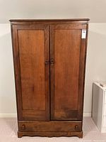 Front view of the closed armoire showing two paneled wooden doors and lower drawer with knobs.