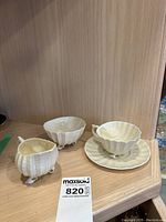 Set of four Belleek China pieces: cup on saucer, cream jug, sugar bowl, each with unique shell feet design.