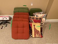 Front view of all patio chair cushions stacked - four green and four orange, with four decorative pillows to the side featuring animal designs including giraffe and zebra