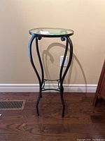 Front view of the black metal frame table with a round glass top standing on wooden floor against a wall.