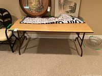 Rectangular folding table with wood veneer top surface and metal folding legs; shown in a room against a wall with other furniture.