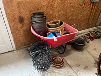Pink wheelbarrow holding assorted plant pots and blue watering can