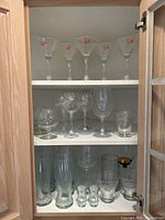 Full cabinet shelf view showing all glassware arranged with martini glasses on top shelf and variety of stemware on middle shelf plus beer and shot glasses on bottom shelf.