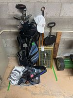Photo of the golf bag with clubs inside showing bag, club covers, white golf cap, folding stool, and miscellaneous golf accessories in background.