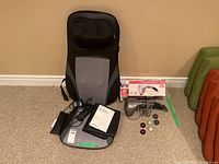 Shiatsu head and back massager with remote control and manual, plus a handheld deep muscle massager and various interchangeable massage heads laid out on carpet.