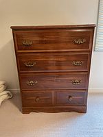 Front view of the wooden highboy dresser showing four drawers with brass handles and knobs.