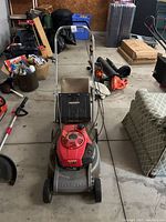 Front view of Honda HR173 lawn mower showing red engine, grey metal deck, and black grass collection bag attached.