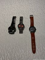 Three men's watches displayed side-by-side on embroidered fabric.