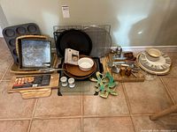 Wide view showing assortment of kitchen items including pans, plates, utensils, and bakeware on tile floor.