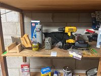 Overall view of the lot on wooden shelving showing drill, propane tank, jars of hardware, saw, and other items.