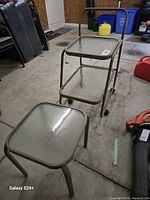 Tempered glass trolley with two shelves and metal frame on wheels, shows wear.