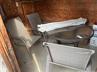 View showing three stacking patio chairs with metal frame and woven mesh seats and backs, round patio table with glass top, and folded white umbrella lying on table