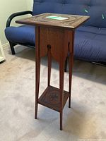 Front angle view of wooden decorative plant stand showing carved surface and lower shelf.