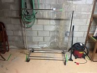 Full front view of a metal portable clothing rack with hanging bar and caster wheels on a concrete floor near a cinder block wall.