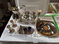 Full view of the water pitcher, four goblets, two candle holders, salt cellars with cobalt glass inserts on a small tray, and serving tongs on oval tray.