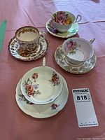 Four floral tea cups and saucers on a pink tablecloth showing variety of floral patterns and gold accents