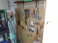 View of assorted hand tools hanging on pegboard including hammers, vice grips, coping saw, tin snips, pliers, scissors, utility knife, and more
