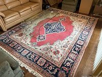 Full view of rug on hardwood floor showing central medallion design, borders, and fringe