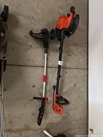 Photo of Black & Decker and Legend Force yard tools lying side by side on garage floor showing both items from above.