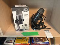Photo of Blue Yeti Nano Premium USB microphone with original box on shelf, microphone placed on built-in stand with attached USB cable.