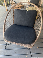 Front view of wicker rattan lounge chair with black seat and back cushions on deck