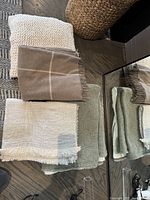 Four assorted blankets and throws in various colors and textures placed on a wooden floor next to a mirror and basket.