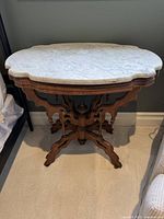 Front quarter view of table showing white marble top and carved wooden base