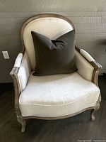 Front view of a linen upholstered armchair showing carved wood frame and charcoal pillow