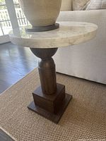 Side angle view of round white marble tabletop with turned wood pedestal base