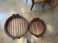 Overhead view of both trays on wood floor beneath dining table chairs showing relative sizes