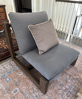 Angled side view showing one chaise chair’s dark wood frame, seat and back cushions, and accent pillow