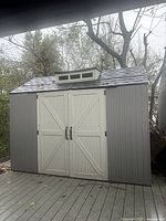 Front view showing grey shed exterior, white doors, roof cupola