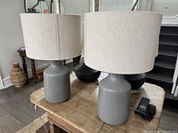 Two gray ceramic table lamps with off-white fabric drum shades on wooden table