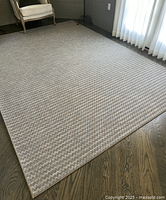 Beige and taupe zigzag patterned area rug laid out on wood floor near chair and curtains