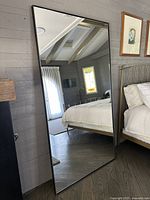 Full-length mirror leaning against wall, reflecting bedroom