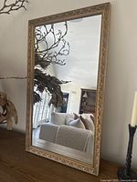 Full front view of the rectangular gold-framed mirror leaning on tabletop, showing overall shape and reflection